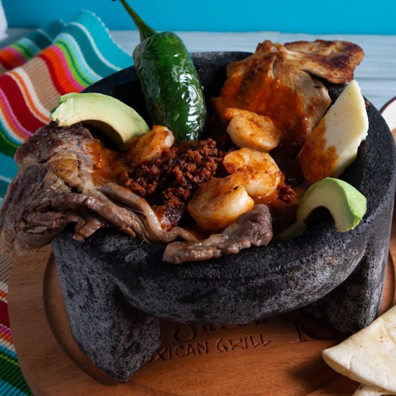 Agavero's Molcajete with steak, shrimp, chorizo, avocado, and cheese, served with tortillas.