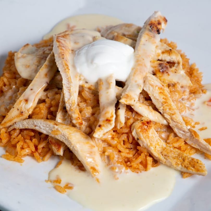 Grilled chicken strips and Mexican rice covered in white cheese sauce and a dollop of sour cream.