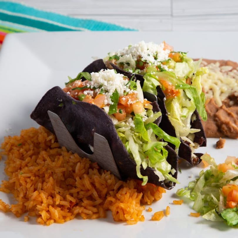 Two Agaveros Mexican Bar and Grill tacos with rice and refried beans on a white plate.